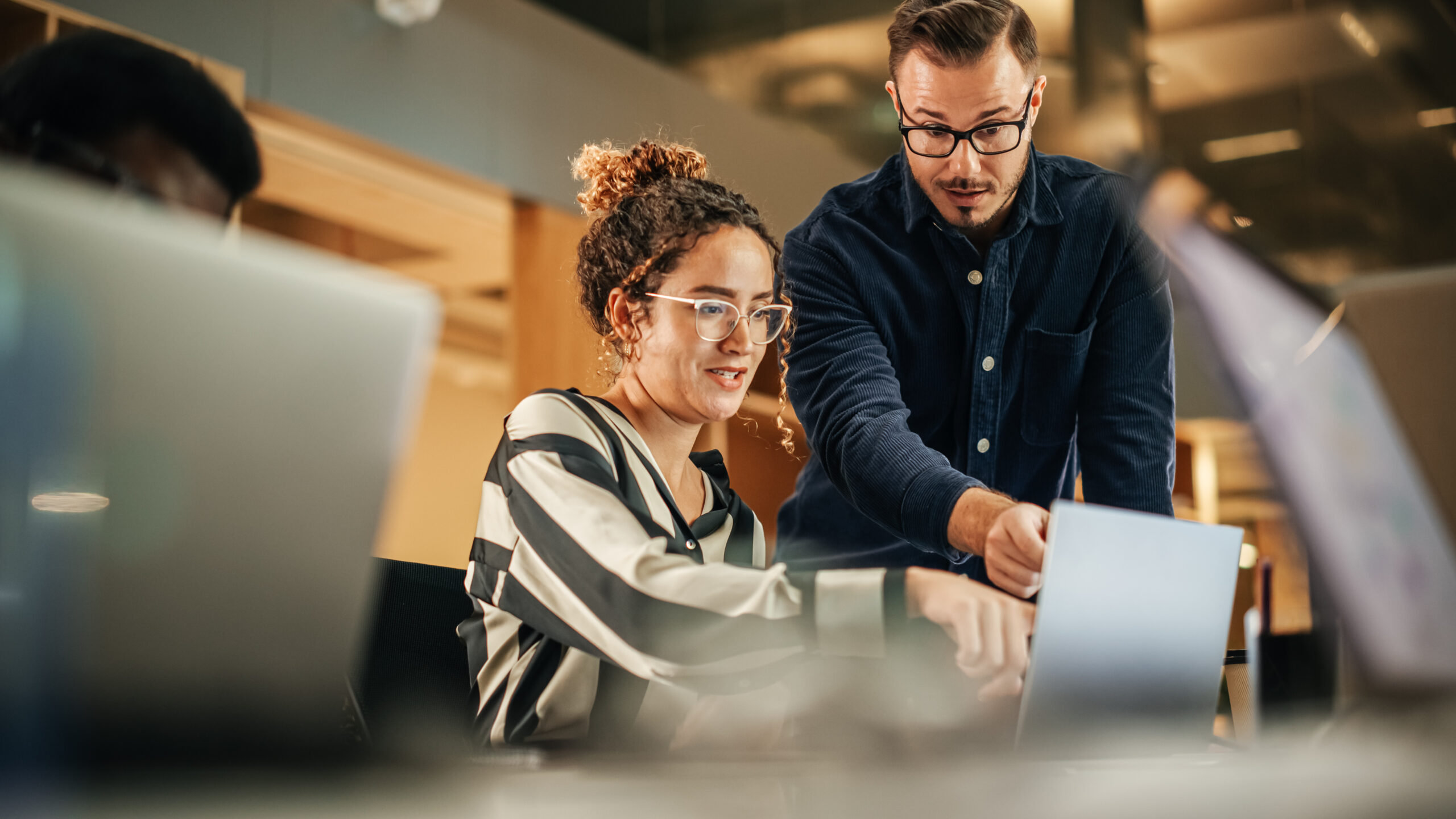 two colleagues working on laptop in office. female hispanic help two colleagues working on laptop in office. female hispanic help